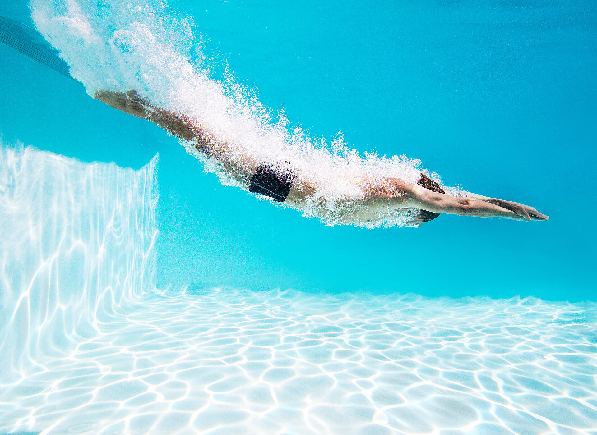 Schwimmer gleitet unter Wasser durch das Hallenbad im Schwimmwerk